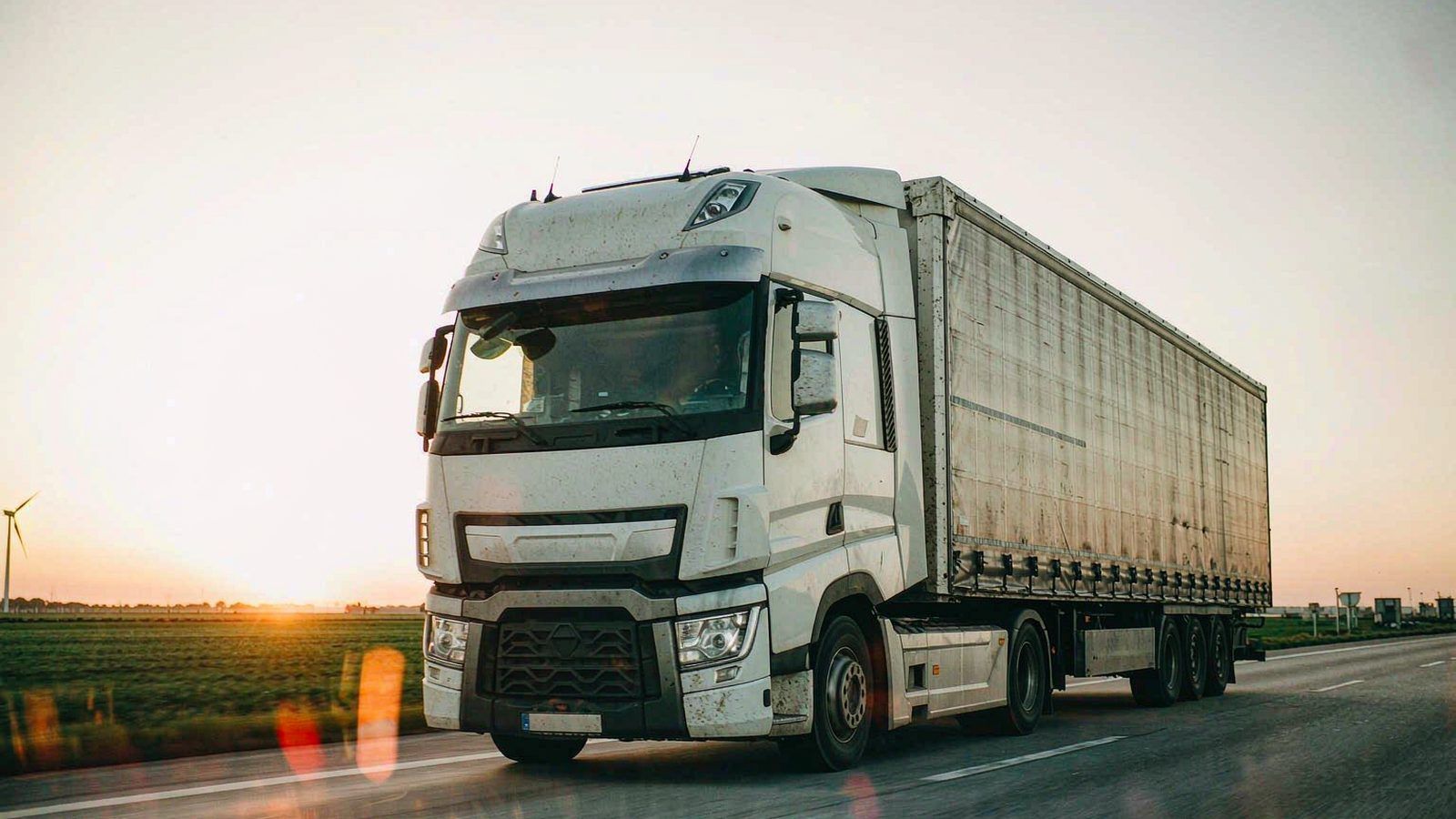 A white cab-over semi-trailer combination on a European motorway at sunrise